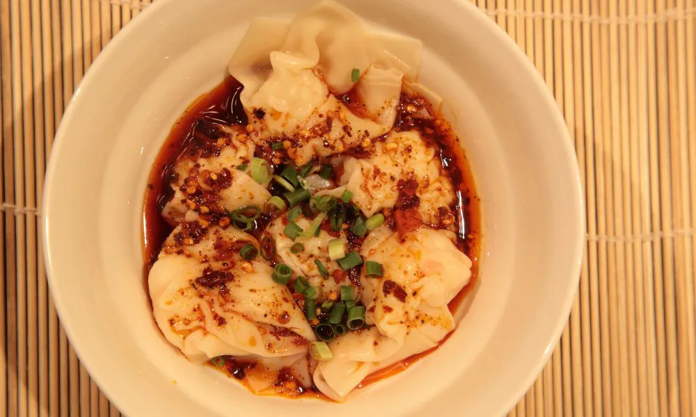 Spicy wontons in red chili oil sauce garnished with green onions at Mingxia Dumpling, a Chinese Restaurant in Cordova