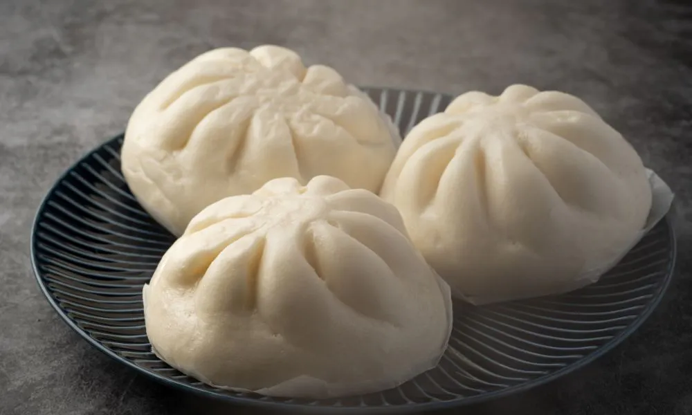 Three steamed pork buns on a dark blue striped plate at Mingxia Dumpling, a Chinese Restaurant in Cordova