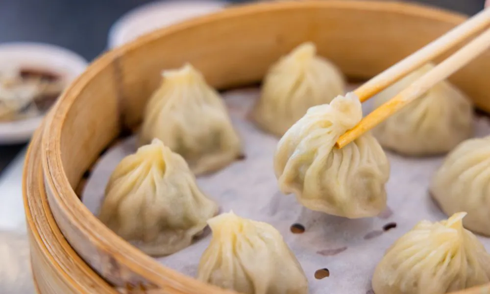 Steamed soup dumplings in a bamboo steamer basket with chopsticks at Mingxia Dumpling, a Chinese Restaurant in Cordova