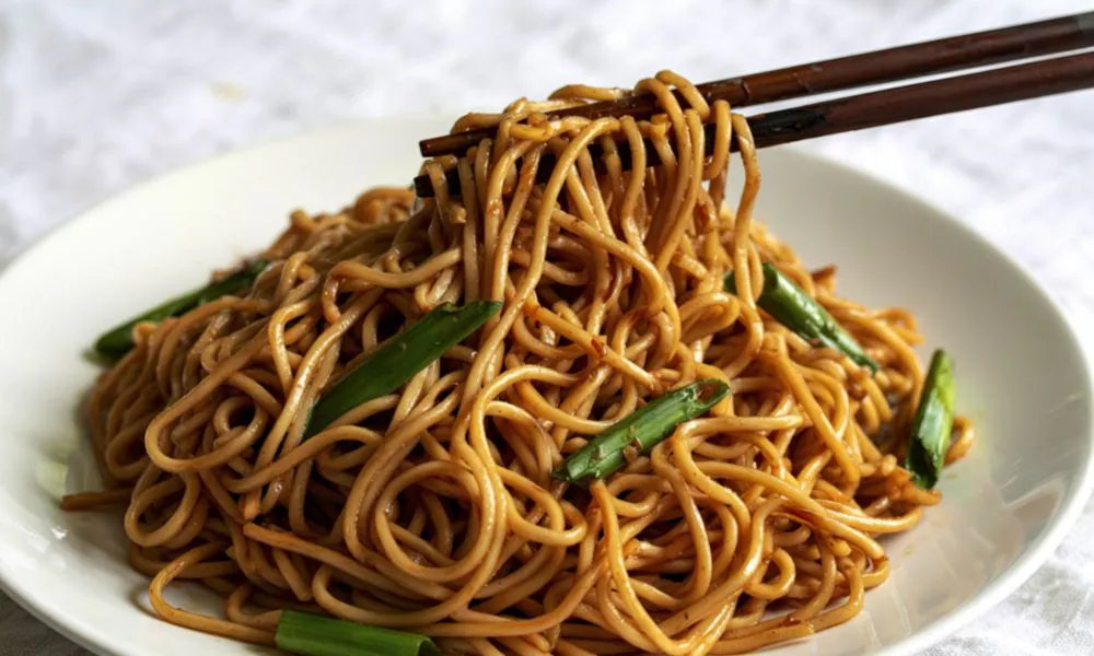 Savory stir-fried noodles with green onions lifted by chopsticks at Mingxia Dumpling, a Chinese Restaurant in Cordova